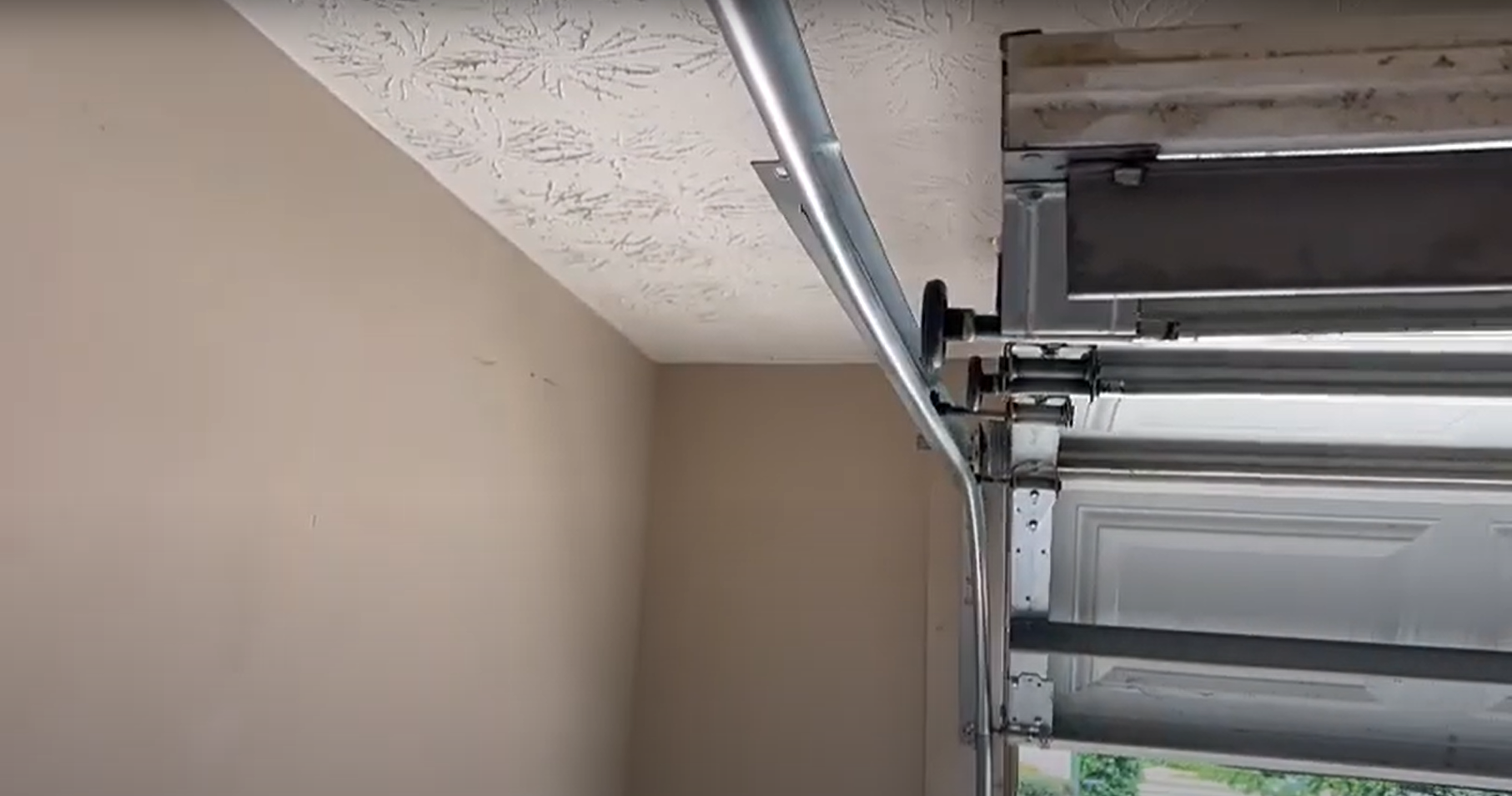 Alt text:performing a garage door track repair on a residential silver metal door.