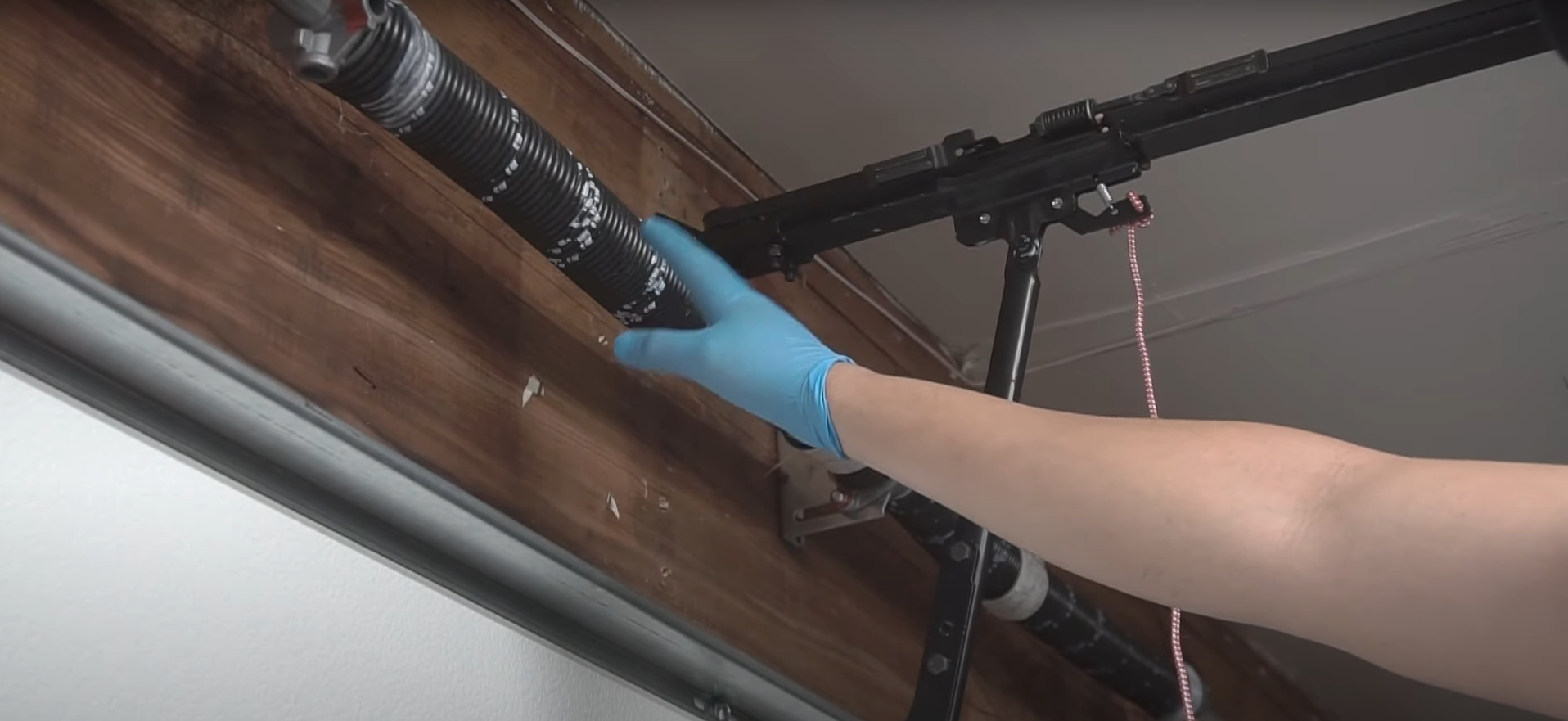 A professional technician repairing a broken garage door spring, with safety glasses on and tools in hand.