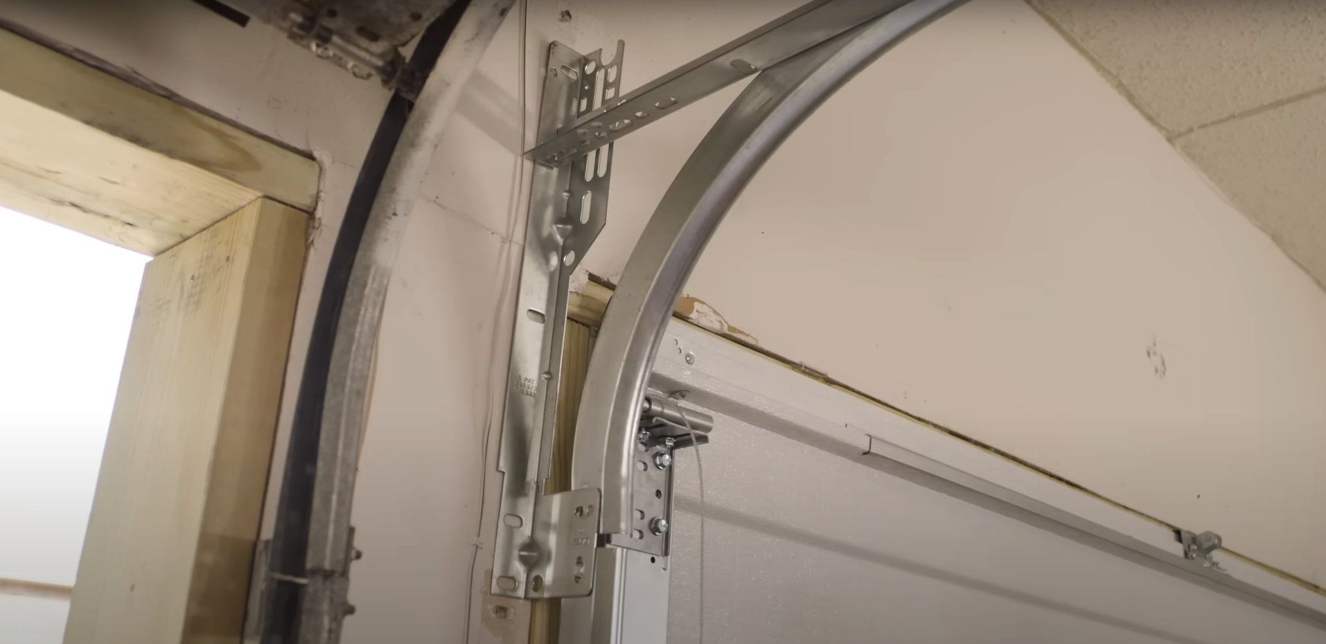 Alt text:performing a garage door track repair on a residential silver metal door.